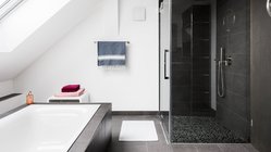 Ein modernes Badezimmer mit einer freistehenden Badewanne und einer eleganten Dusche, die mit dunklen Fliesen gestaltet ist.