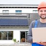 Ein Mann in Arbeitskleidung vor einer Photovoltaikanlage mit einem Laptop in der Hand
