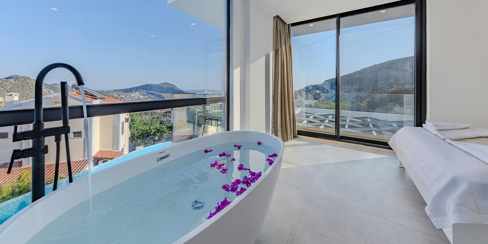 Ein modernes Badezimmer mit einer freistehenden Badewanne, gefüllt mit Wasser und lila Blütenblättern, bietet einen atemberaubenden Ausblick.