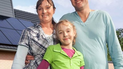 Eine kleine Familie, im Hintergrund ist ein Haus mit einer Photovoltaikanlage